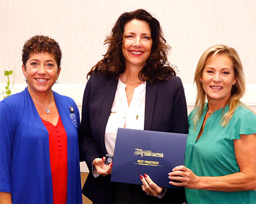 FCCC Best Practices Committee Chair Laura E. Roth, Esq., (left) and 2020-2021 FCCC President Tara S. Green (right) presents St. Lucie County Clerk and Comptroller Michelle R. Miller with a Recognition of Excellence certificate